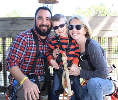 Colin, a young boy with Angelman Syndrome and his mother and father pose for a picture during an outdoor adventure