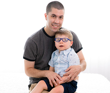 Mason, a young boy with Angelman Syndrome sits on his father’s lap
